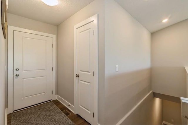 hallway with dark wood-style flooring, a textured ceiling, and baseboards