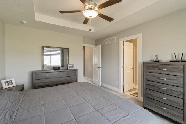 bedroom with baseboards, connected bathroom, visible vents, and a tray ceiling