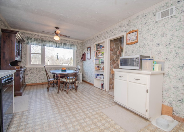 dining space featuring ceiling fan, visible vents, baseboards, wallpapered walls, and crown molding