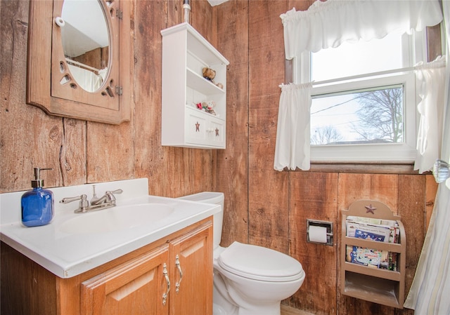 bathroom with toilet, wood walls, and vanity