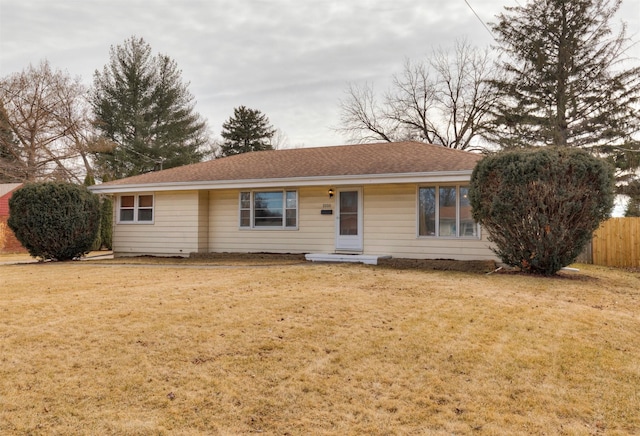 ranch-style house featuring a shingled roof, a front yard, and fence