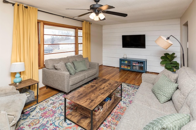 living room with wooden walls, wood finished floors, and ceiling fan