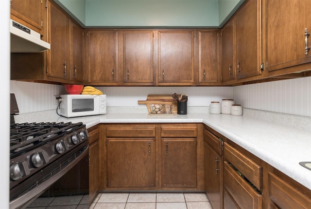 kitchen featuring under cabinet range hood, white microwave, light countertops, and range with gas cooktop