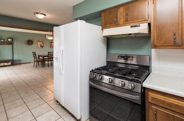 kitchen with light tile patterned floors, under cabinet range hood, light countertops, stainless steel gas range, and brown cabinets