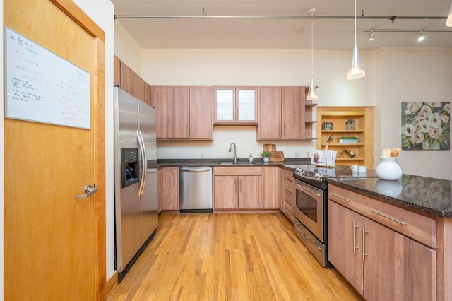 kitchen with stainless steel appliances, a sink, light wood-style floors, open shelves, and dark stone countertops