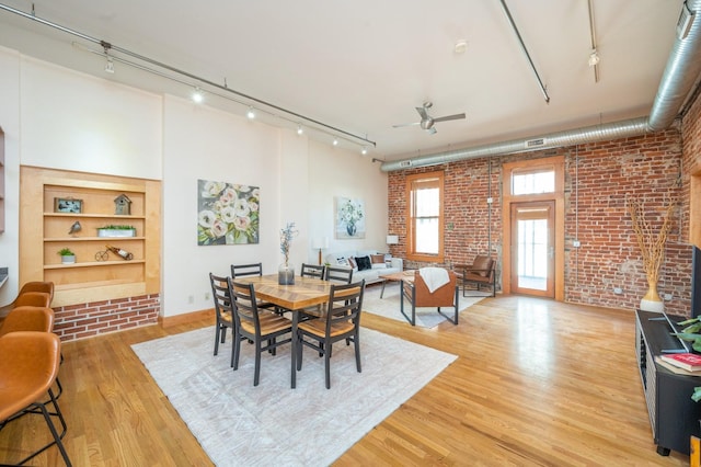 dining space with brick wall, light wood-type flooring, and rail lighting