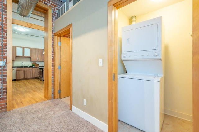 laundry room featuring stacked washer and dryer, light carpet, a sink, and baseboards