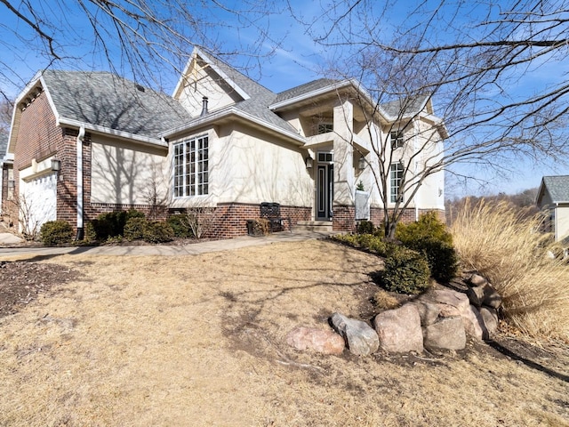 view of side of home with a garage, brick siding, a shingled roof, and stucco siding