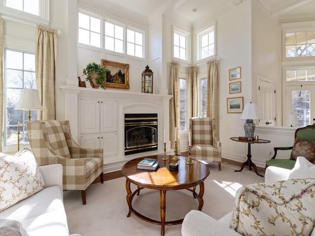 living room featuring a wealth of natural light, a glass covered fireplace, crown molding, and a towering ceiling