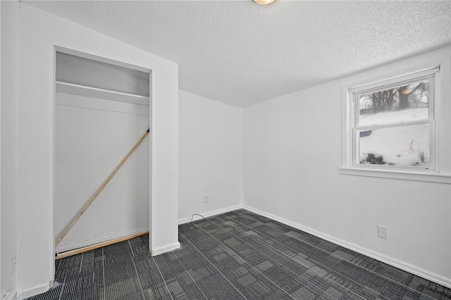 unfurnished bedroom featuring baseboards, dark colored carpet, and a textured ceiling