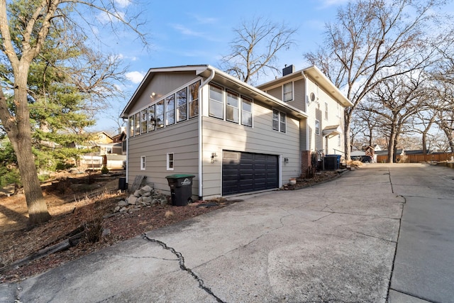 view of side of home with a garage, driveway, a chimney, and central AC unit