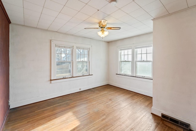 unfurnished room with a ceiling fan, wood finished floors, visible vents, and baseboards