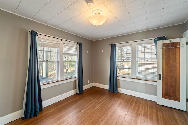 spare room with crown molding, wood finished floors, and baseboards