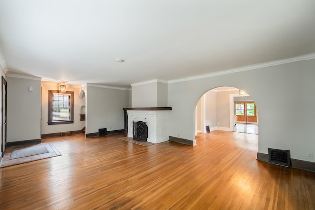 6015 Waterbury Cir, Des Moines, IA 50312 - unfurnished living room featuring arched walkways, light wood-style flooring, a brick fireplace, crown molding, and baseboards