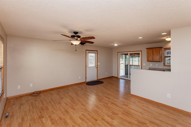 unfurnished living room featuring baseboards, a textured ceiling, visible vents, and light wood-style floors