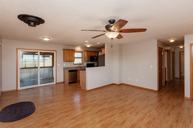 unfurnished living room featuring a textured ceiling, a sink, light wood-style flooring, and baseboards