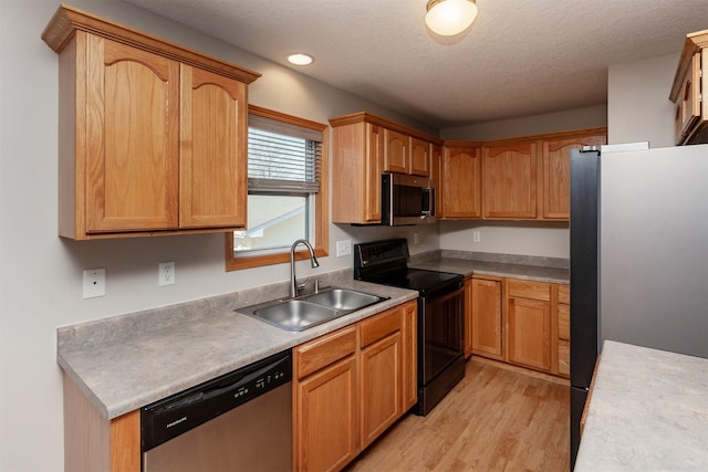 kitchen featuring light countertops, appliances with stainless steel finishes, a sink, a textured ceiling, and light wood-type flooring