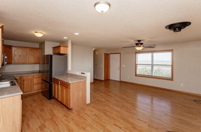 kitchen featuring stainless steel microwave, freestanding refrigerator, a textured ceiling, light wood-type flooring, and baseboards