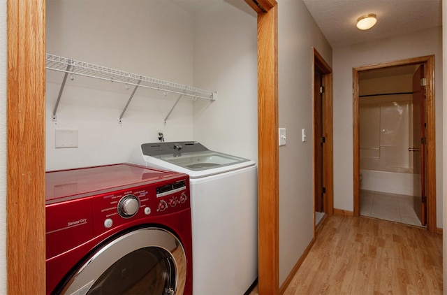 clothes washing area featuring light wood-type flooring, washer and dryer, laundry area, and baseboards