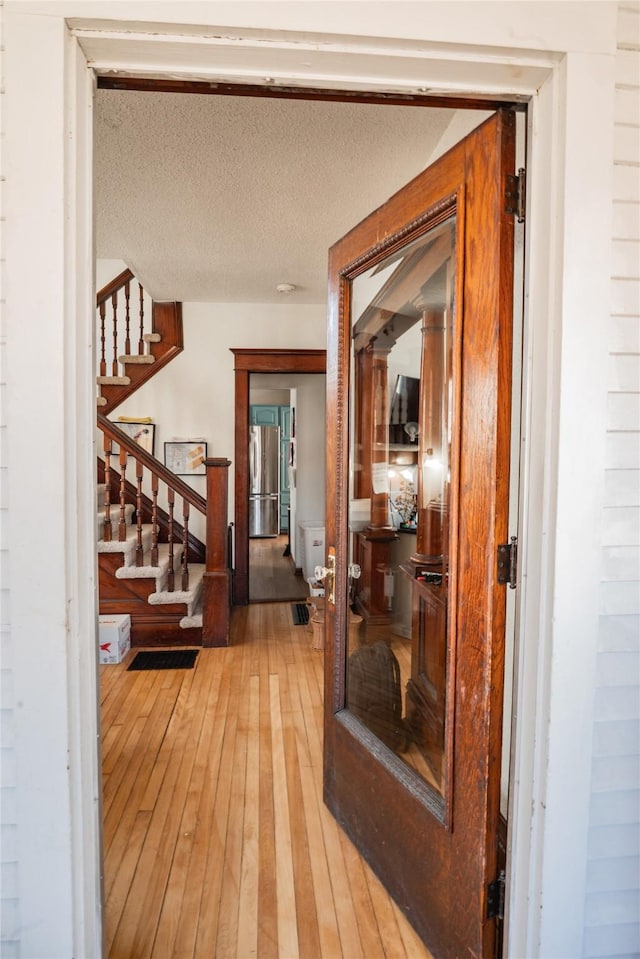 hallway with stairway, light wood-style flooring, and a textured ceiling