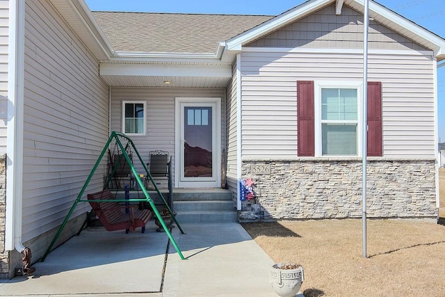 doorway to property featuring stone siding and a shingled roof