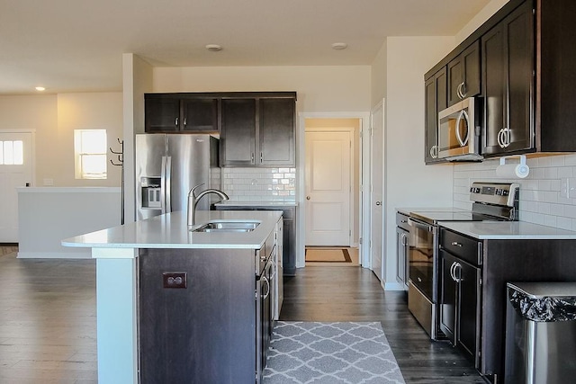 kitchen featuring a kitchen island with sink, stainless steel appliances, a sink, light countertops, and dark wood-style floors