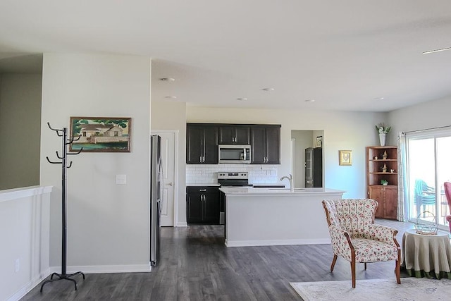 kitchen featuring light countertops, appliances with stainless steel finishes, dark cabinetry, decorative backsplash, and dark wood-style floors