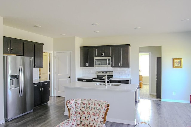 kitchen featuring light countertops, appliances with stainless steel finishes, decorative backsplash, dark wood-style floors, and an island with sink