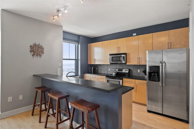 kitchen with a breakfast bar, stainless steel appliances, decorative backsplash, light wood-type flooring, and a peninsula