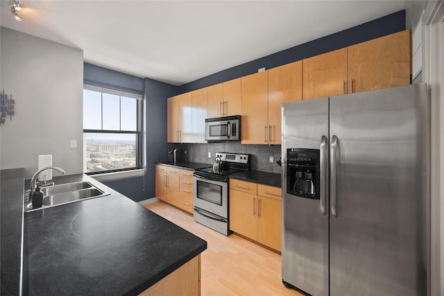 kitchen with dark countertops, light wood-style flooring, appliances with stainless steel finishes, a sink, and backsplash