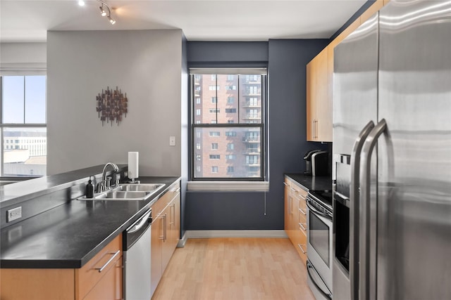 kitchen featuring light wood finished floors, dark countertops, appliances with stainless steel finishes, light brown cabinets, and a sink