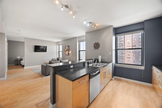 kitchen featuring light wood-style flooring, a peninsula, a sink, stainless steel dishwasher, and dark countertops