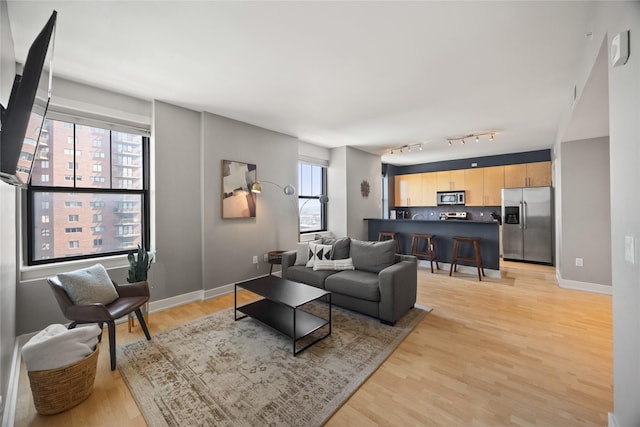 living area featuring track lighting, light wood-style flooring, and baseboards