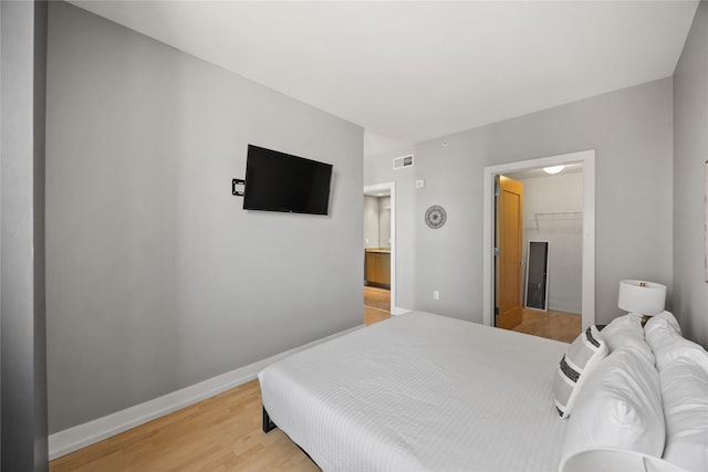 bedroom with a closet, visible vents, a spacious closet, light wood-type flooring, and baseboards