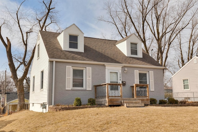 new england style home featuring roof with shingles, brick siding, and a front lawn