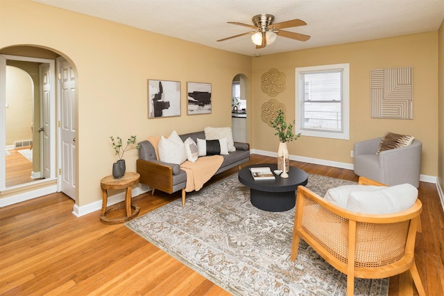 living room featuring arched walkways, ceiling fan, visible vents, baseboards, and light wood finished floors