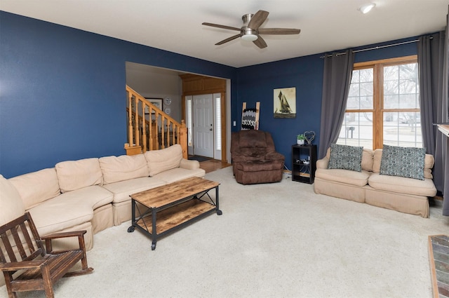 carpeted living area with a ceiling fan and stairs