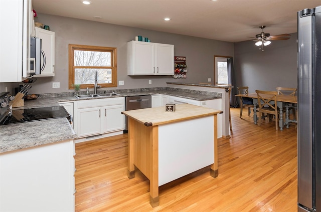 kitchen with stainless steel appliances, white cabinets, a sink, light wood-type flooring, and a peninsula