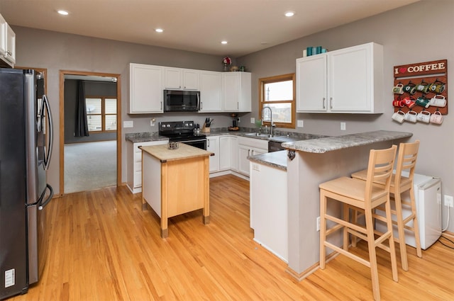 kitchen with a sink, a kitchen island, white cabinetry, appliances with stainless steel finishes, and light wood finished floors