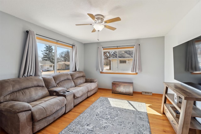 living area featuring light wood-style flooring, a ceiling fan, visible vents, and baseboards