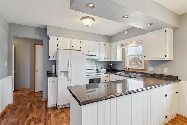 kitchen with wood finished floors, a peninsula, white appliances, and a sink