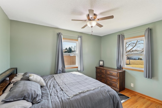 bedroom with a textured ceiling, wood finished floors, a ceiling fan, and baseboards