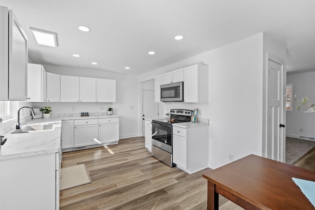 kitchen featuring light wood-style flooring, a sink, recessed lighting, appliances with stainless steel finishes, and white cabinets