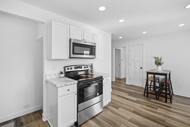 kitchen with light wood finished floors, baseboards, recessed lighting, white cabinets, and stainless steel appliances