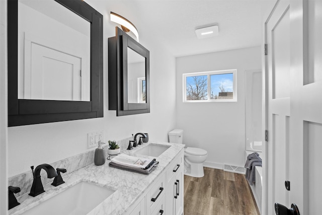 bathroom featuring toilet, wood finished floors, visible vents, and a sink