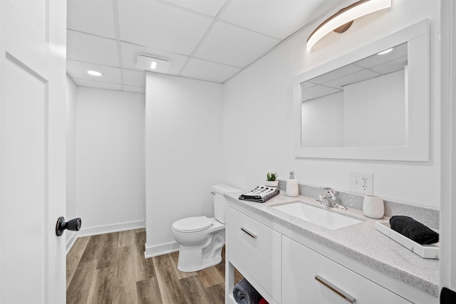 bathroom featuring vanity, wood finished floors, baseboards, a paneled ceiling, and toilet