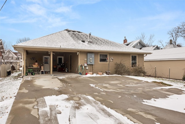 snow covered property featuring a shingled roof and fence