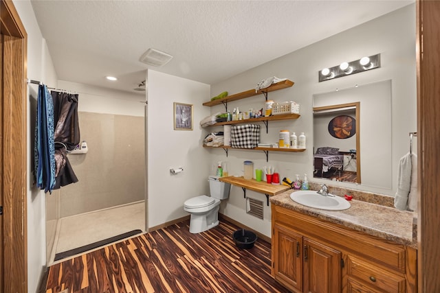 full bathroom featuring wood finished floors, toilet, vanity, a textured ceiling, and a walk in shower