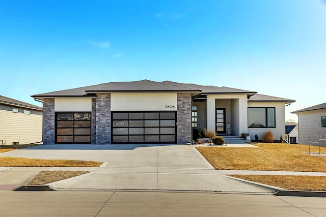 prairie-style home featuring a garage, concrete driveway, stone siding, and stucco siding