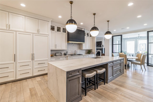 kitchen with glass insert cabinets, a kitchen island with sink, light wood-style flooring, and a breakfast bar area